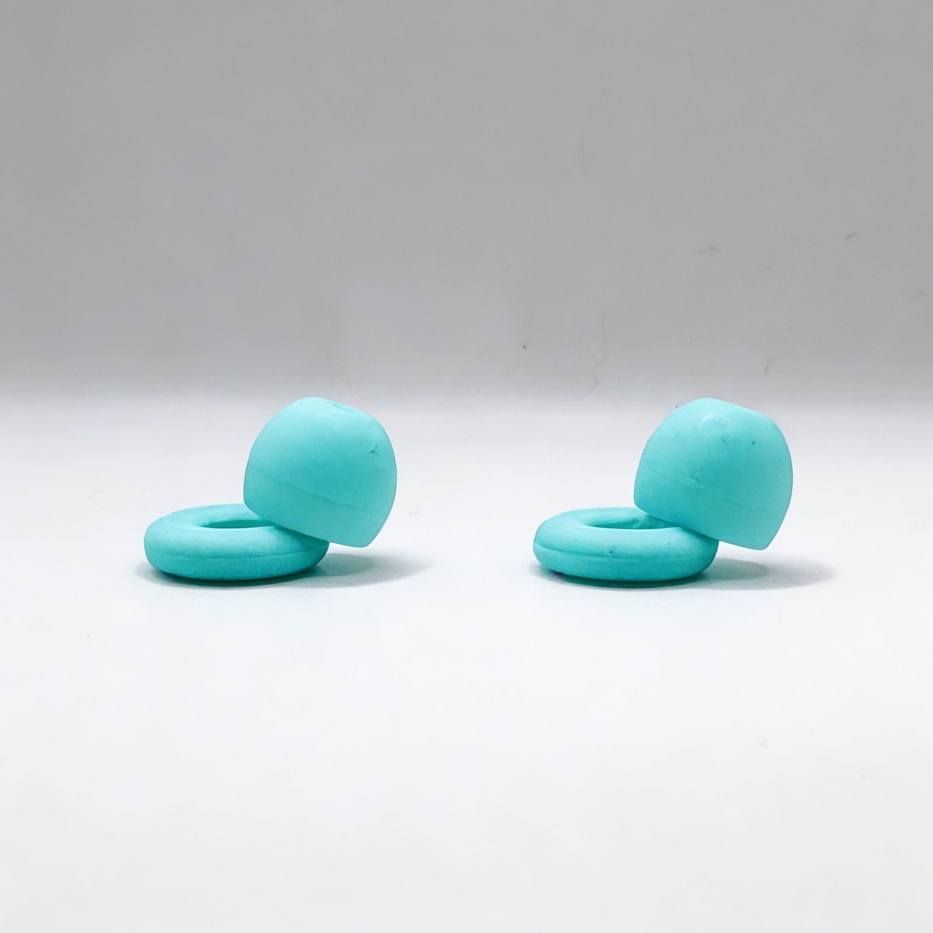 Two turquoise rubber ollybuds on a white background